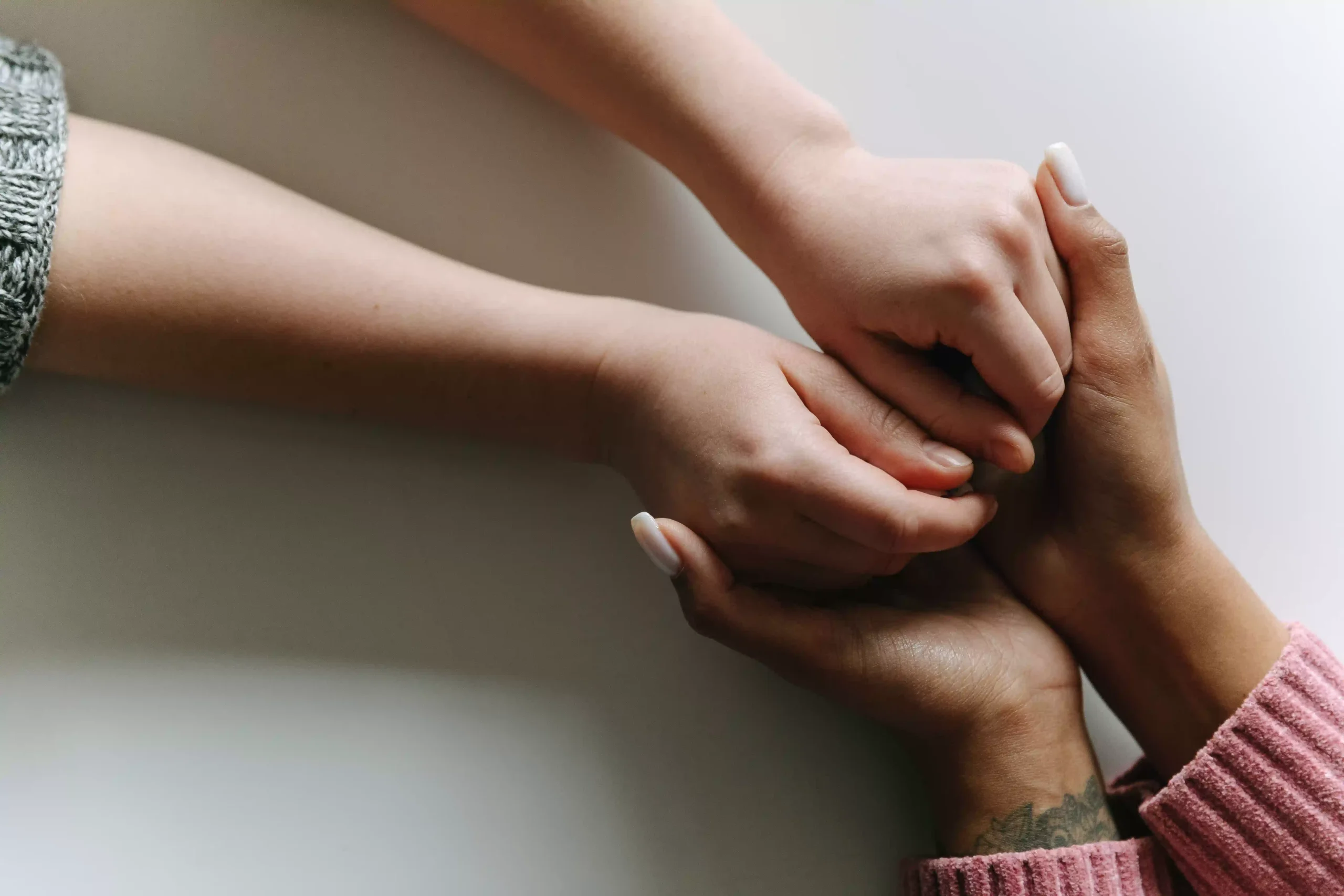 Manos de una mujer mayor y de una mujer joven entrelazadas sobre una mesa de madera