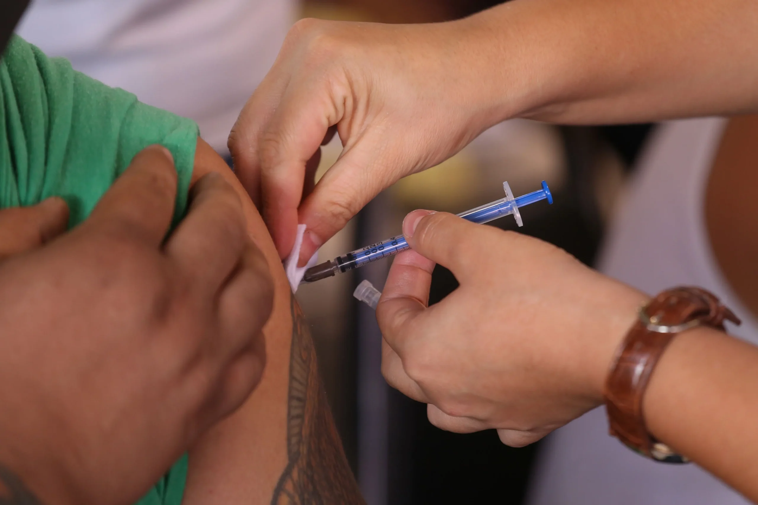 Enfermera aplica una vacuna en el brazo de un adulto joven en un módulo de salud